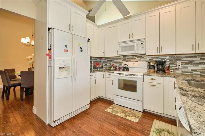 Kitchen with white cabinetry, white appliances, tasteful backsplash, and dark wood-style floors