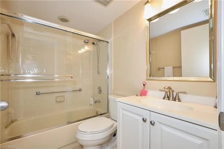 Bathroom featuring toilet, shower / bath combination with glass door, visible vents, and vanity