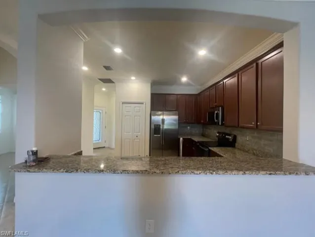 Kitchen with backsplash, a peninsula, light stone counters, and stainless steel appliances