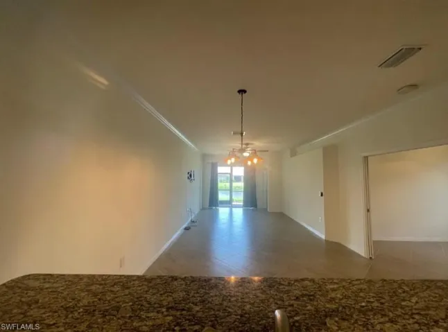 Tiled empty room with ornamental molding, visible vents, baseboards, and a chandelier