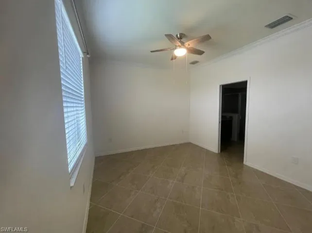 Tiled spare room with crown molding, baseboards, a ceiling fan, and visible vents
