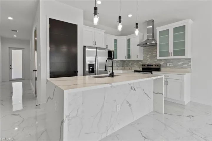 Kitchen with light marble finish floors, wall chimney range hood, stainless steel appliances, tasteful backsplash, and recessed lighting