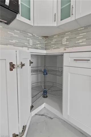 Kitchen view of white cabinets, light countertops, black microwave, and decorative backsplash