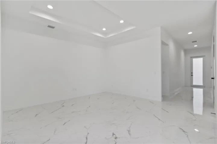 Empty room with recessed lighting, marble finish floors, and a tray ceiling