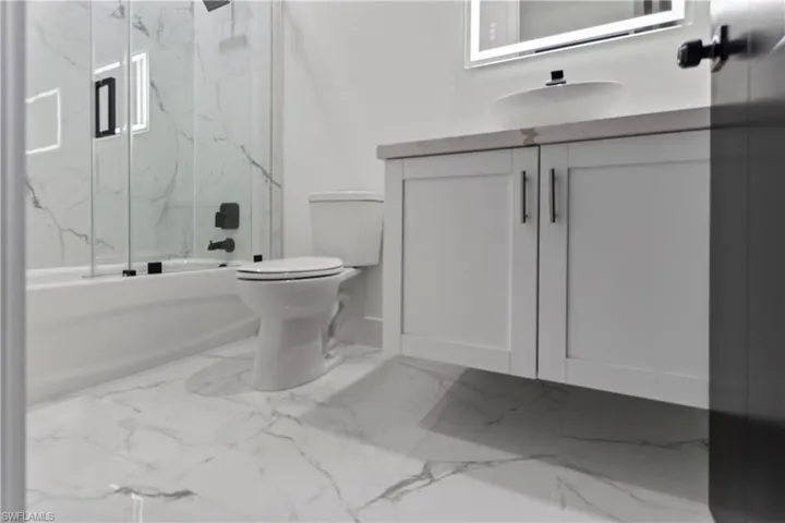 Full bath featuring vanity, combined bath / shower with glass door, and marble finish flooring