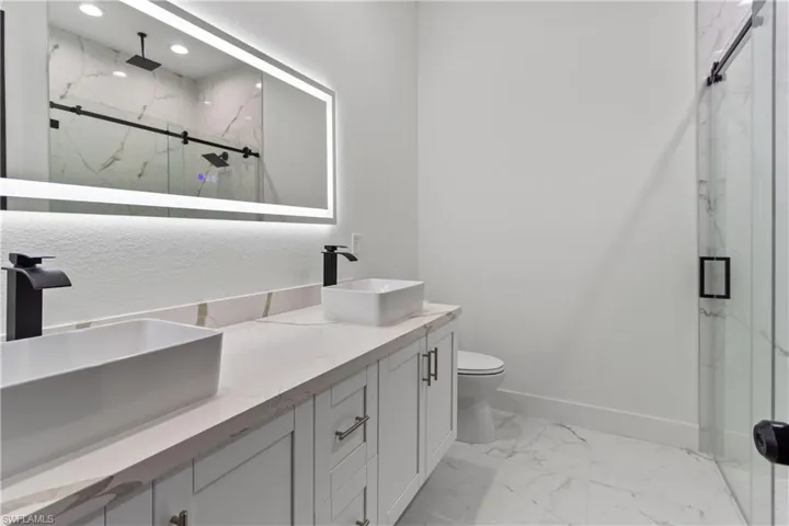 Bathroom with marble look tile flooring, a marble finish shower, double vanity, and recessed lighting