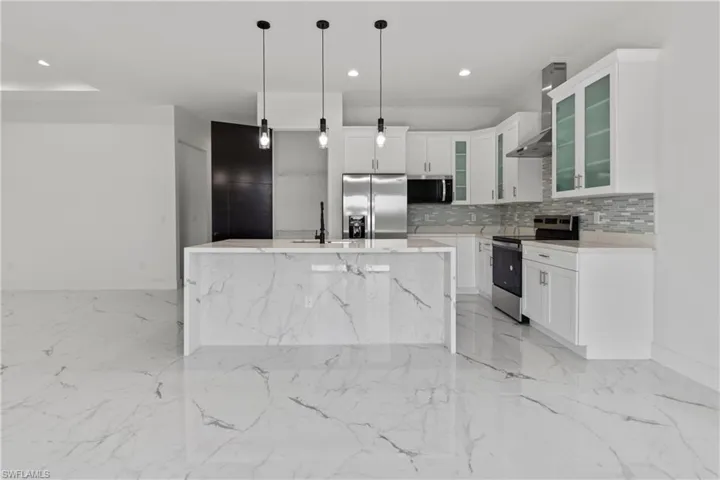 Kitchen with appliances with stainless steel finishes, wall chimney exhaust hood, light marble finish flooring, light countertops, and tasteful backsplash