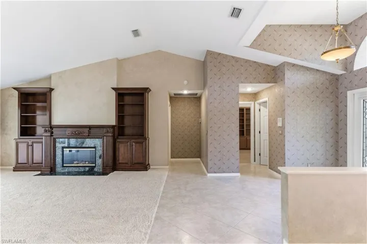 Unfurnished living room featuring lofted ceiling, a high end fireplace, light tile patterned floors, and wallpapered walls
