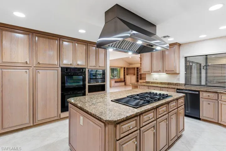Kitchen featuring light stone countertops, a center island, island range hood, black appliances, and light tile patterned flooring