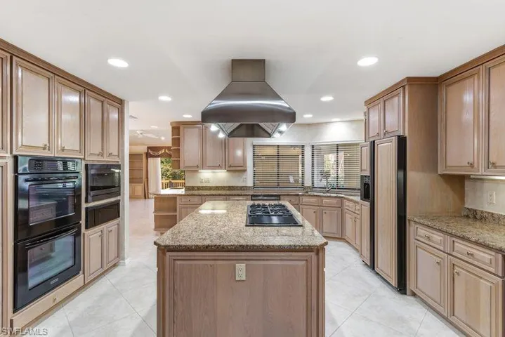 Kitchen featuring a kitchen island, light stone counters, built in appliances, open shelves, and recessed lighting
