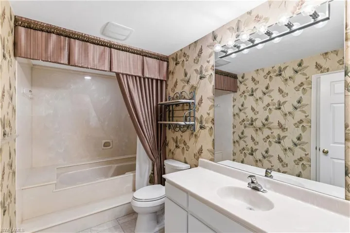 Bathroom with vanity, wallpapered walls, light tile patterned floors, and shower / bath combo with shower curtain