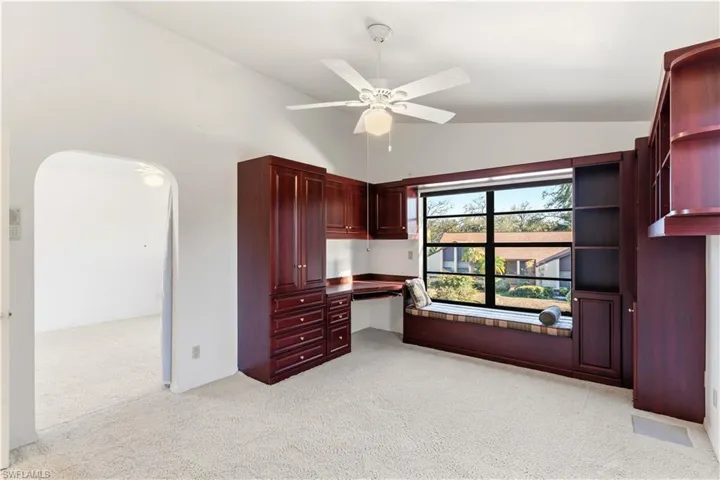 upstairs Bedroom/office with built in study area, light colored carpet, vaulted ceiling, a ceiling fan, and arched walkways