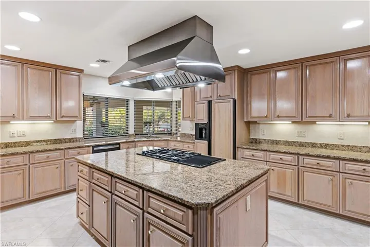 Kitchen featuring light stone countertops, a center island, island range hood, paneled refrigerator, and recessed lighting