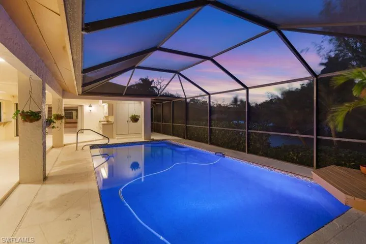 Pool at dusk with an outdoor pool, glass enclosure, a sunroom, and a patio area