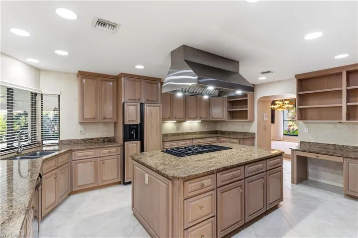 Kitchen with exhaust hood, a center island, light stone counters, open shelves, and paneled built in refrigerator