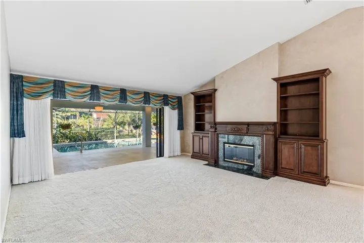 Unfurnished living room with vaulted ceiling, light colored carpet, built in features, a fireplace, and a sunroom