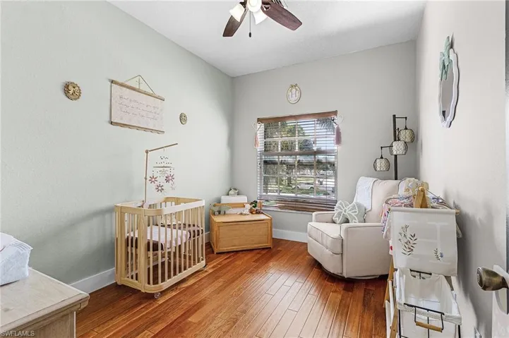 Bedroom with a crib, wood-type flooring, and a ceiling fan