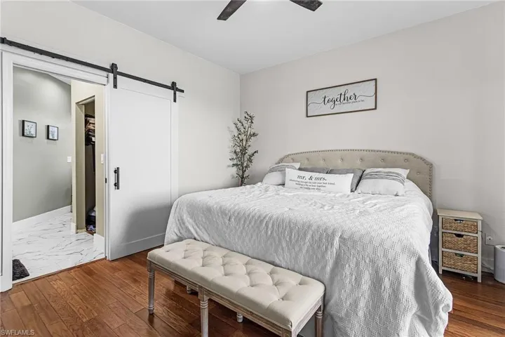 Bedroom with a barn door, dark wood-style floors, and ceiling fan