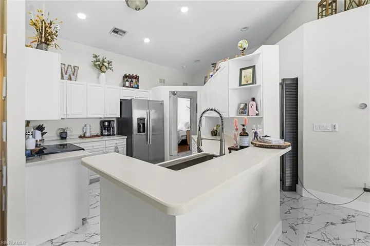Kitchen with light marble finish flooring, stainless steel fridge with ice dispenser, white cabinets, light countertops, and recessed lighting