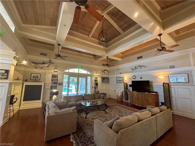 Living area featuring ceiling fan, a decorative wall, coffered ceiling, dark wood-style flooring, and beamed ceiling