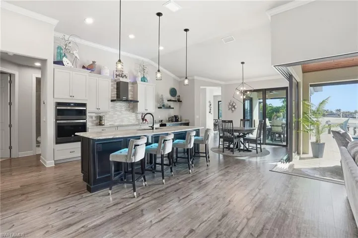 Kitchen featuring white cabinets, pendant lighting, ornamental molding, a kitchen breakfast bar, and wall chimney range hood
