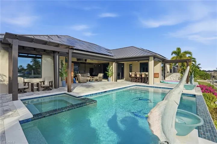 Back of property featuring a patio area, a pool with connected hot tub, outdoor dining area, a pergola, and roof mounted solar panels