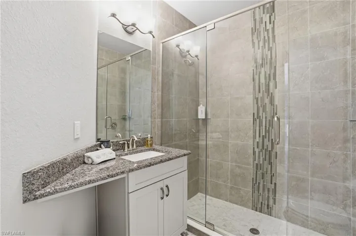 Bathroom with vanity, a textured wall, and a shower stall