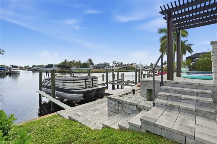 Dock area with boat lift, a water view, a pergola, and a patio