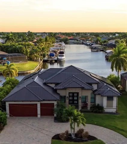 View of front of property featuring a water view, a garage, a decorative circular driveway, and a metal roof.