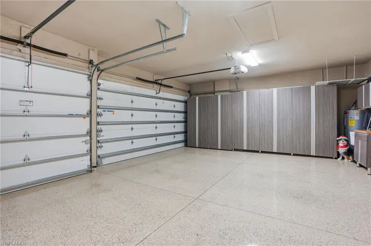 Garage featuring a water heater, a garage door opener, cabinets, and epoxy floors.