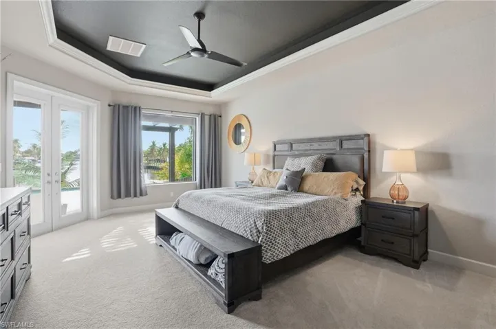 Bedroom featuring a raised ceiling, access to outside, light colored carpet, ceiling fan and water views