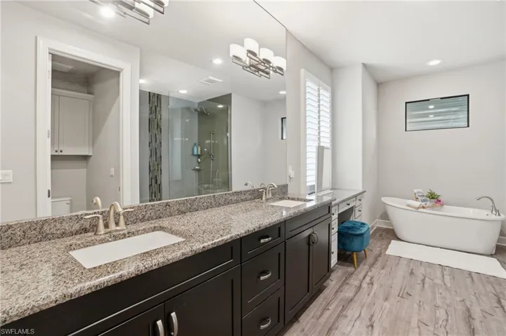 Bathroom with double vanity, make up vanity, walk-in shower, a freestanding soaking bath tub, light wood-style floors, and recessed lighting