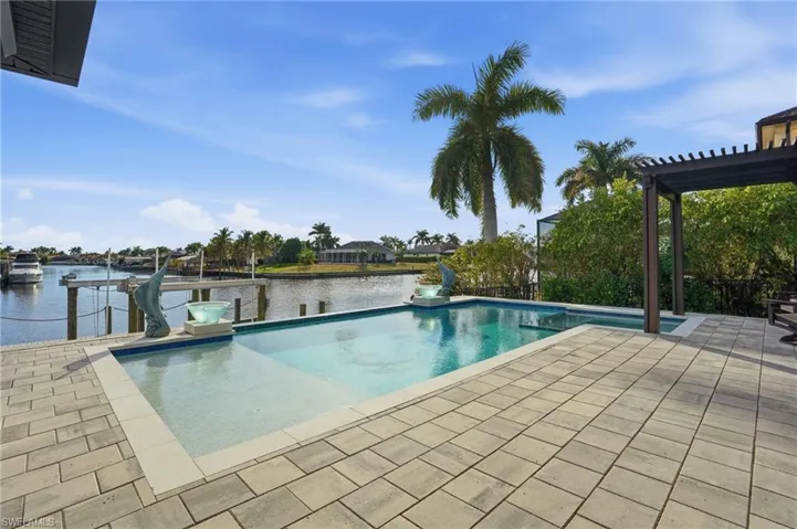 Pool with sunshelf and built-in spa looking onto the water, spacious pool deck- patio area, a pergola, a dock, and a boat lift