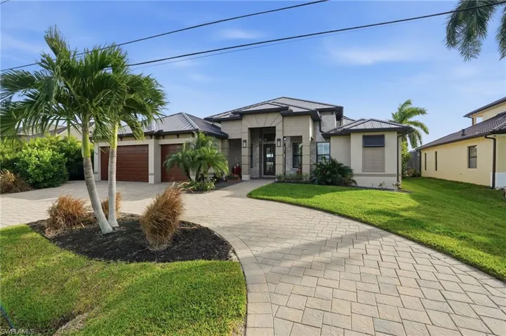 View of front facade featuring a front yard, decorative driveway, a metal roof, and three car garage.