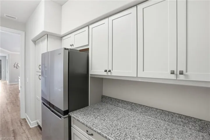 Butler pantry featuring a refrigerator, white cabinetry, light stone counters, and light wood finished floors