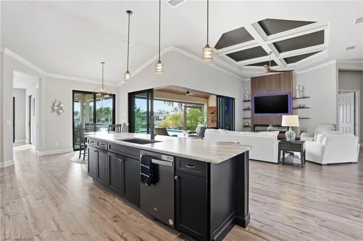 Kitchen with dark cabinets, decorative light fixtures, open floor plan, ornamental molding, and coffered ceiling