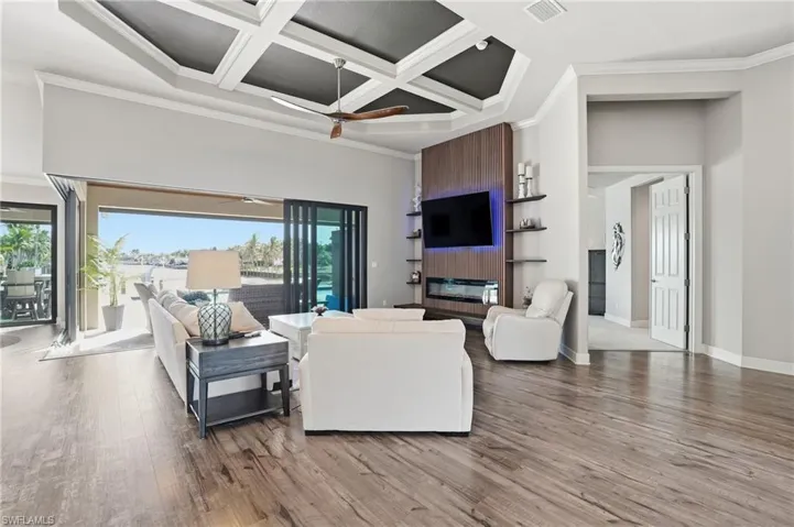 Living area featuring coffered ceiling, ornamental molding, beamed ceiling, wood finished floors, a fireplace, and zero-edge sliders.