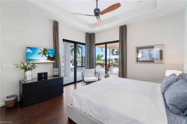 Bedroom with a tray ceiling, access to exterior, ceiling fan, and dark wood-type flooring