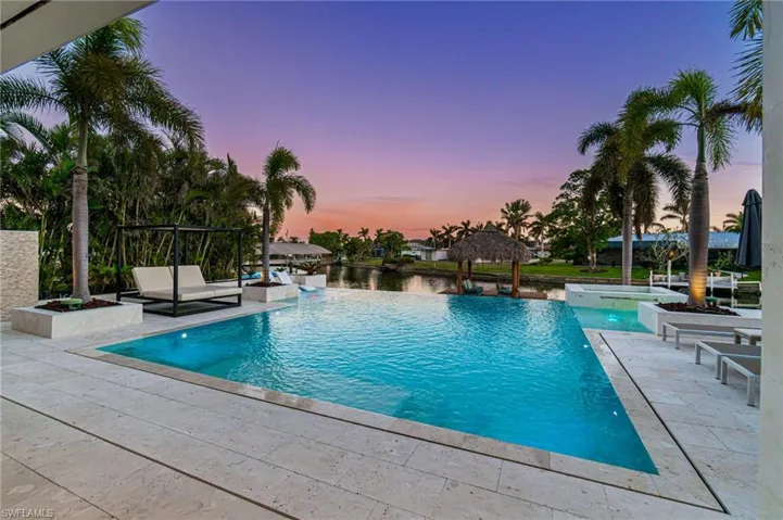 Pool at dusk featuring a gazebo, a water view, a patio, and a hot tub