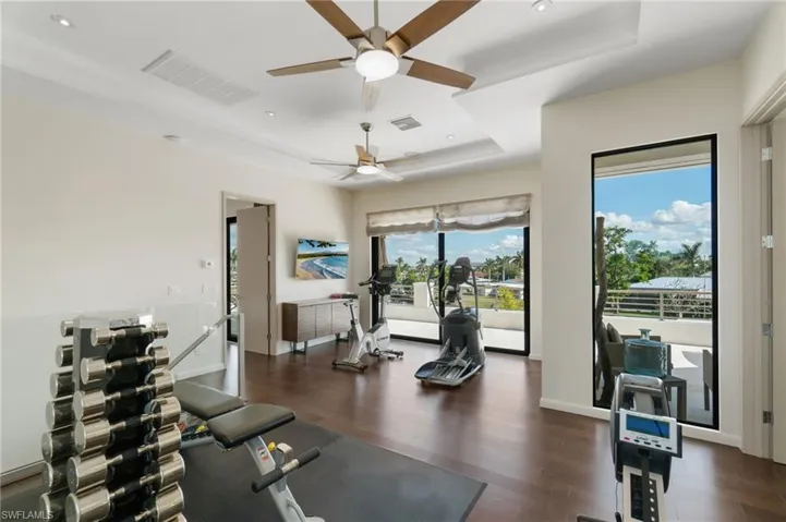 Exercise area with a raised ceiling, ceiling fan, and dark hardwood / wood-style floors