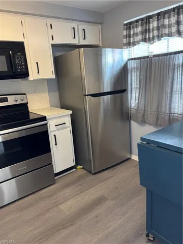 Kitchen featuring range, stainless steel fridge, white cabinets, light countertops, and wood finished floors
