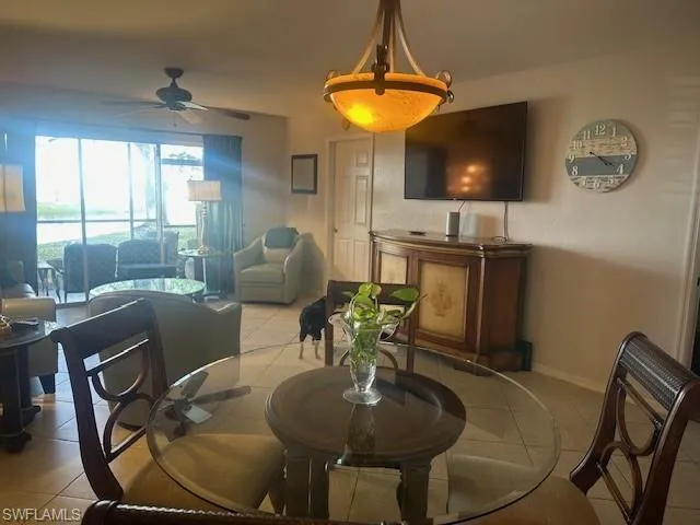Dining room to living room with tile floors, large screen TV and a ceiling fan