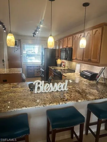 View of Kitchen featuring stone counters, stove, a kitchen bar, and deluxe freestanding refrigerator with tap to see inside feature window