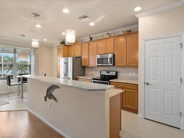 Kitchen featuring ornamental molding, decorative light fixtures, stainless steel appliances, a center island, and decorative backsplash