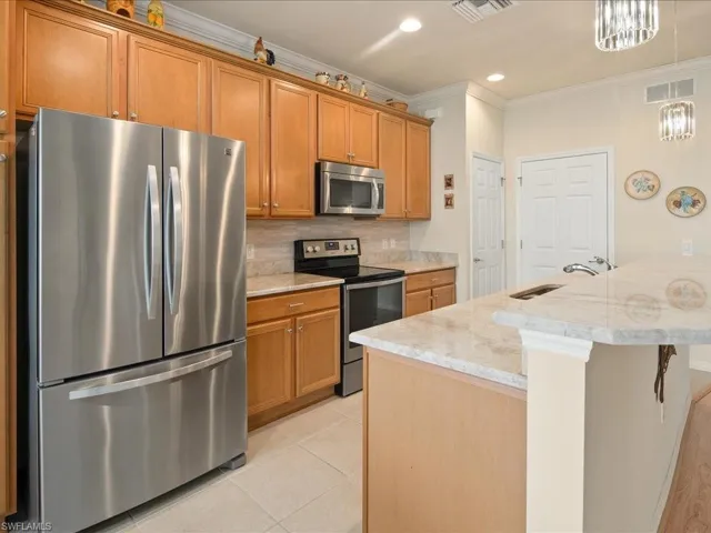Kitchen featuring tasteful backsplash, appliances with stainless steel finishes, decorative light fixtures, ornamental molding, and light stone countertops