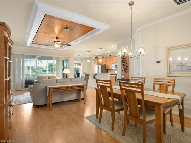 Dining area featuring a tray ceiling, ceiling fan with notable chandelier, light hardwood / wood-style flooring, ornamental molding, and wooden ceiling