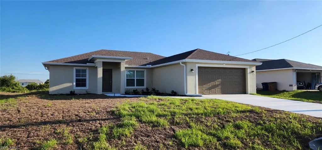 Ranch-style home with concrete driveway, stucco siding, a garage, roof with shingles, and a front lawn