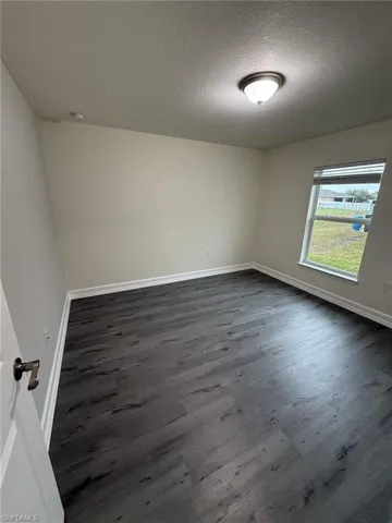 Unfurnished room featuring dark wood-type flooring and a textured ceiling