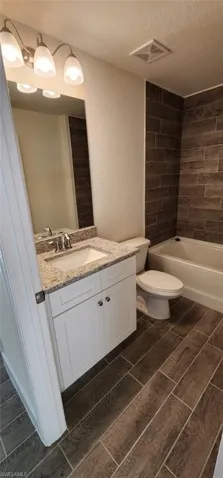 Full bath featuring wood finish floors, vanity, a textured wall, a textured ceiling, and shower / washtub combination