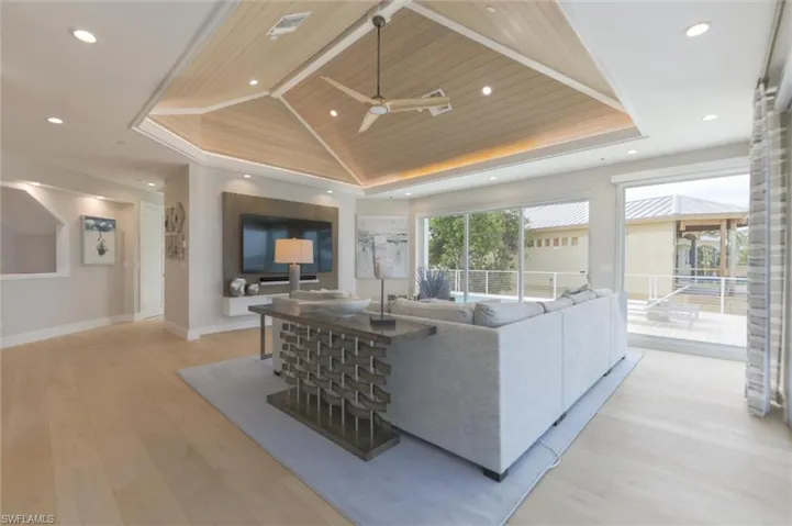 Living room with ceiling fan, a raised ceiling, light wood-type flooring, and wooden ceiling